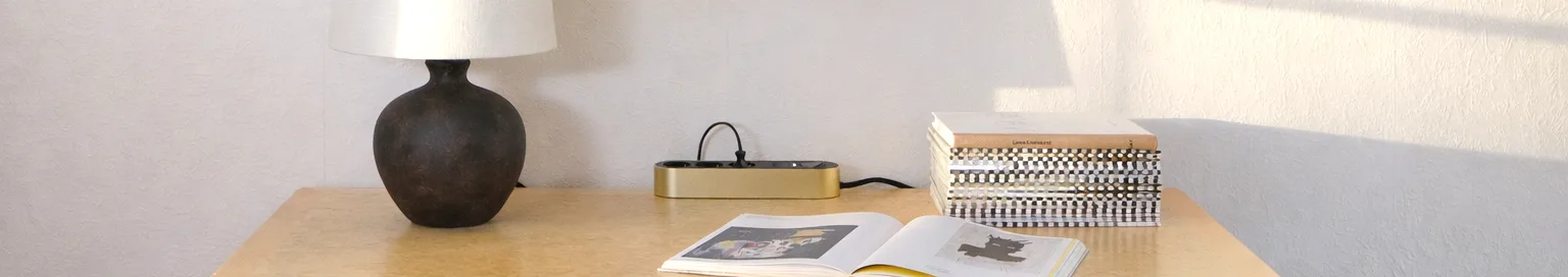 밝은 표면에 놓인 세 개의 검은색 콘센트와 전원 버튼이 있는 금색 멀티탭.