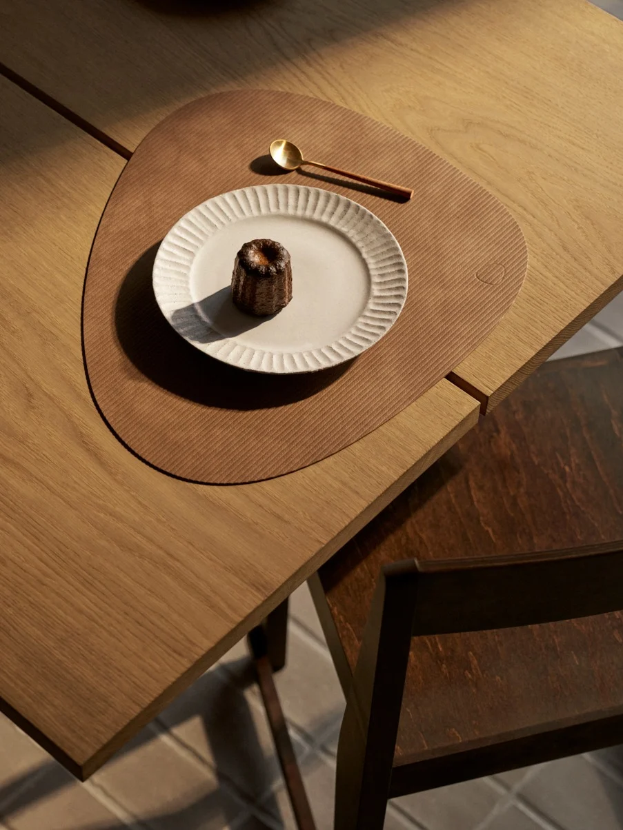 위에서 본 모습: 흰 접시에 담긴 카눌레, 금색 숟가락, 질감 있는 갈색 매트, 나무 테이블.