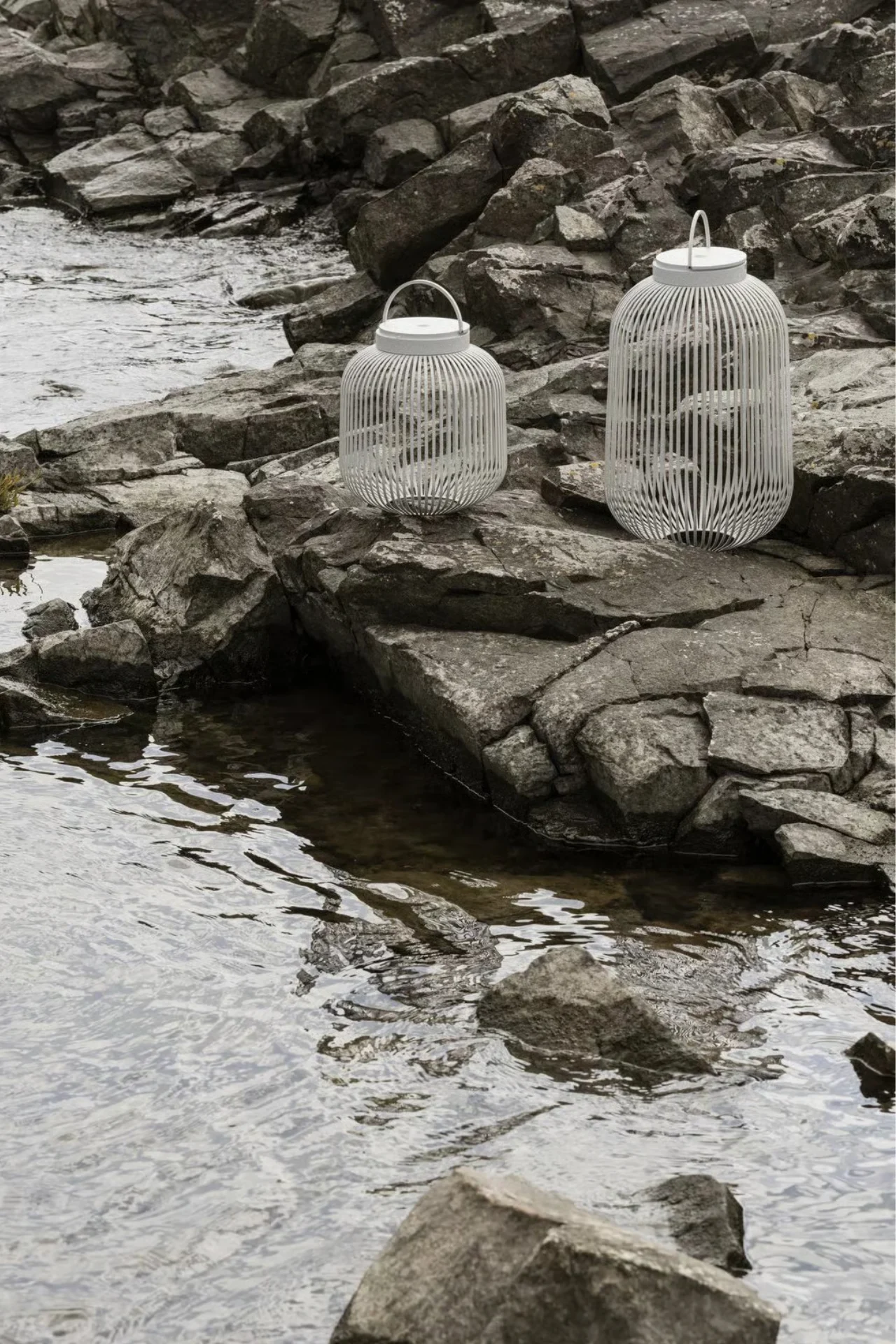 흐르는 시냇물 옆 어두운 바위 위에 손잡이가 있는 흰색 살구조 랜턴 두 개.