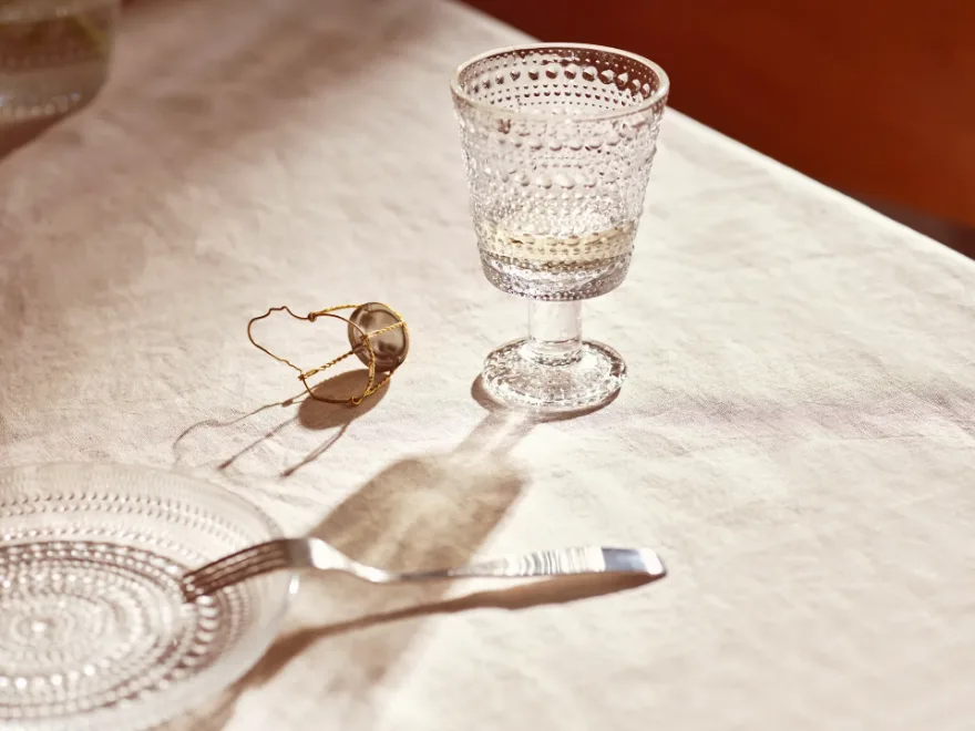 무늬 있는 유리잔, 샴페인 코르크, 포크가 밝은 식탁보 위에 놓여 있고 강한 그림자가 드리워져 있습니다.