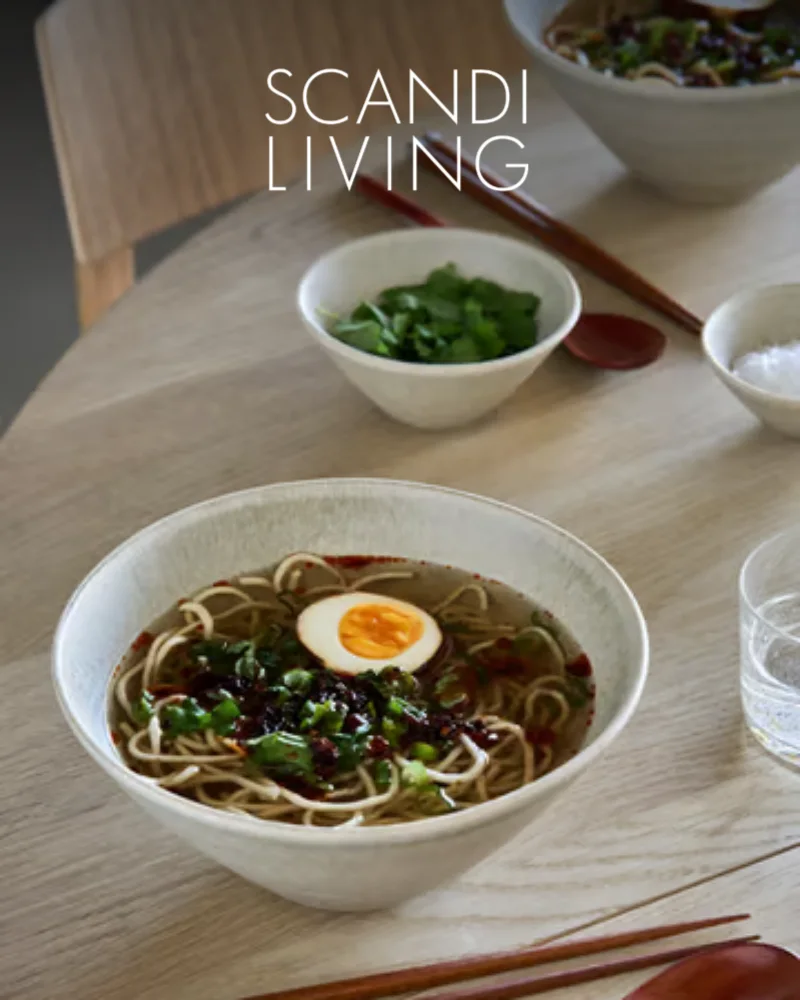 달걀, 파, 고추기름을 곁들인 라면 한 그릇과 젓가락이 나무 테이블 위에 놓여 있고, 'SCANDI LIVING' 텍스트가 있다.