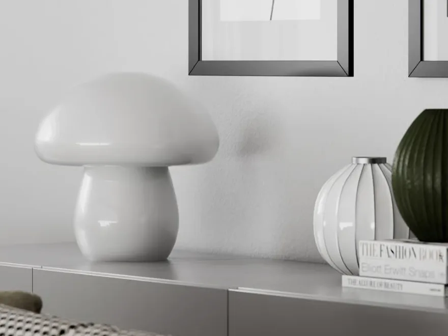 하얀 버섯 모양 램프가 회색 찬장 위에 놓여 있으며, 흰색 골이 있는 꽃병, 짙은 녹색 골이 있는 꽃병, 그리고 책들이 옆에 있습니다.