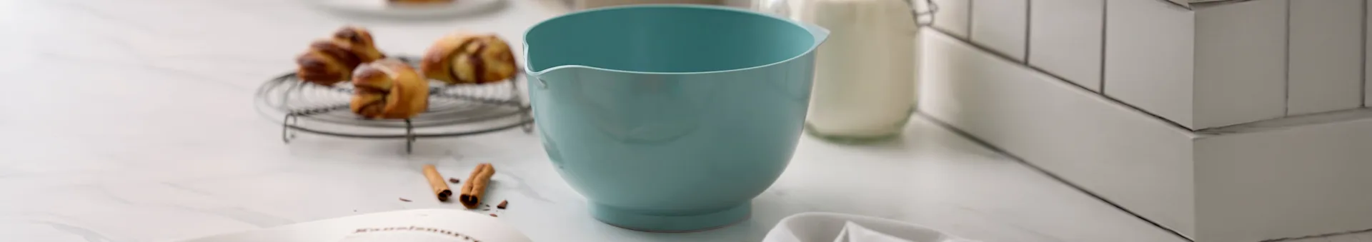 하늘색 믹싱 볼, 선반 위의 페이스트리, 우유병, 대리석 조리대 위의 레시피 책.