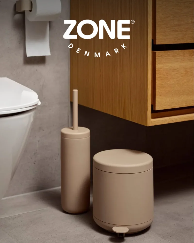 모던한 욕실에 변기, 나무 캐비닛과 무광 베이지 변기솔, 페달 휴지통. ZONE DENMARK 로고.