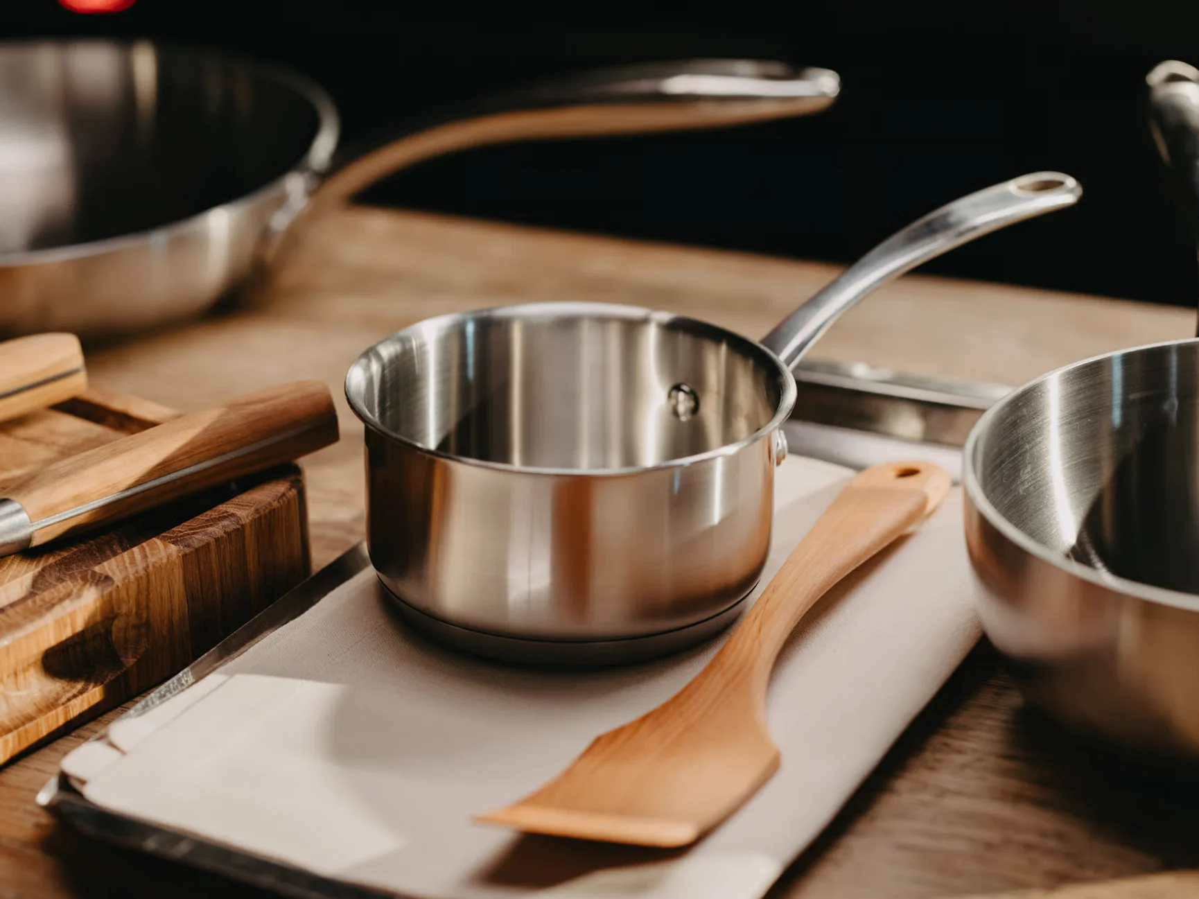 스테인리스 스틸 냄비와 나무 주걱이 다른 주방용품과 함께 베이지색 천 위에 놓여 있습니다.