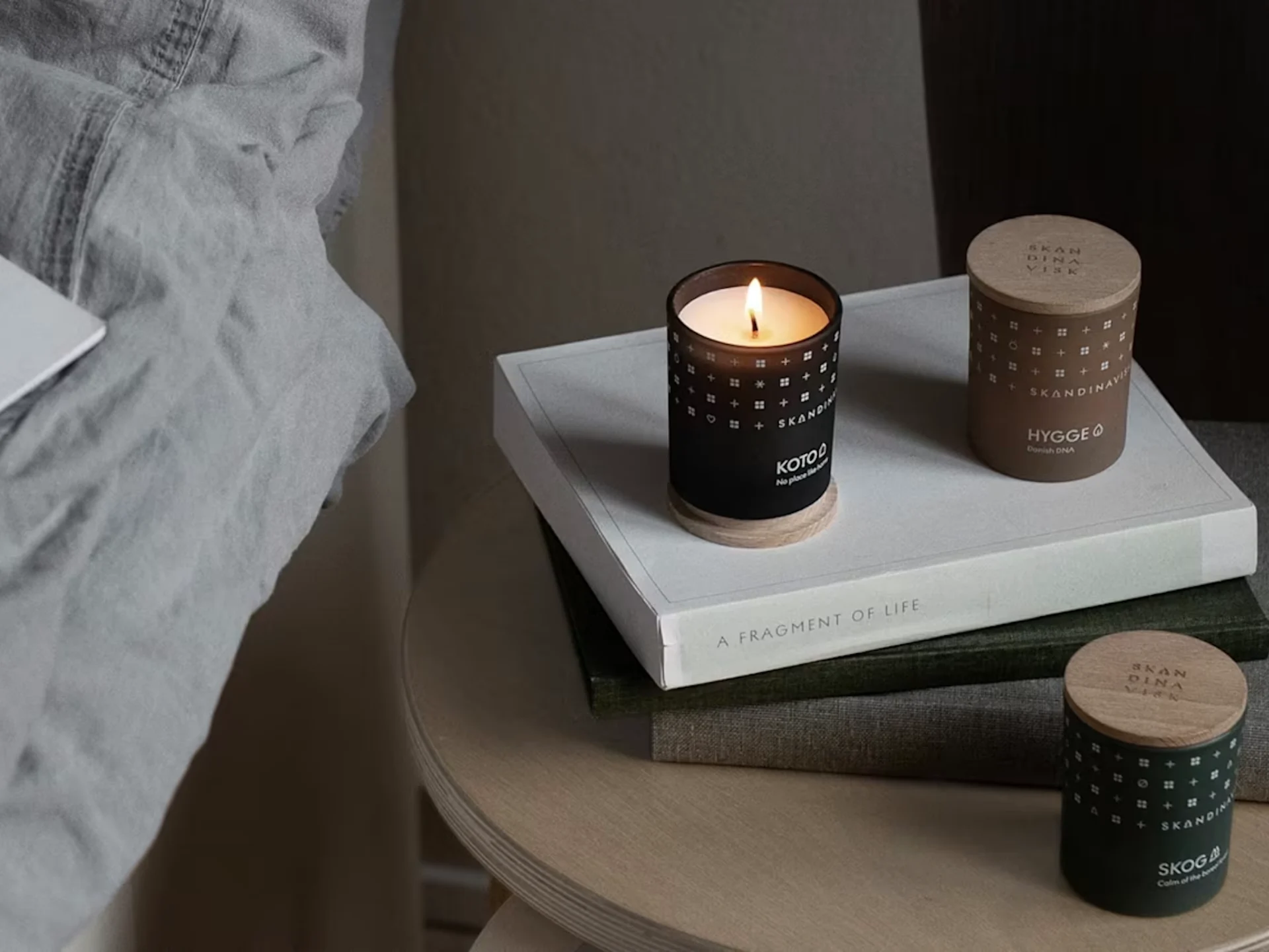 침대 옆 책 위에 놓인 스칸디나비아 스타일 향초 3개, 검은색 촛불 한 개에 불이 켜져 있습니다.