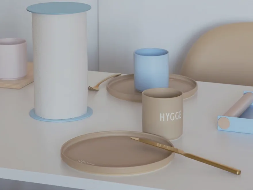 밝은 파란색 키친타월 홀더, 베이지색 접시, 'HYGGE' 문구가 있는 머그컵과 금색 나이프가 놓인 테이블.