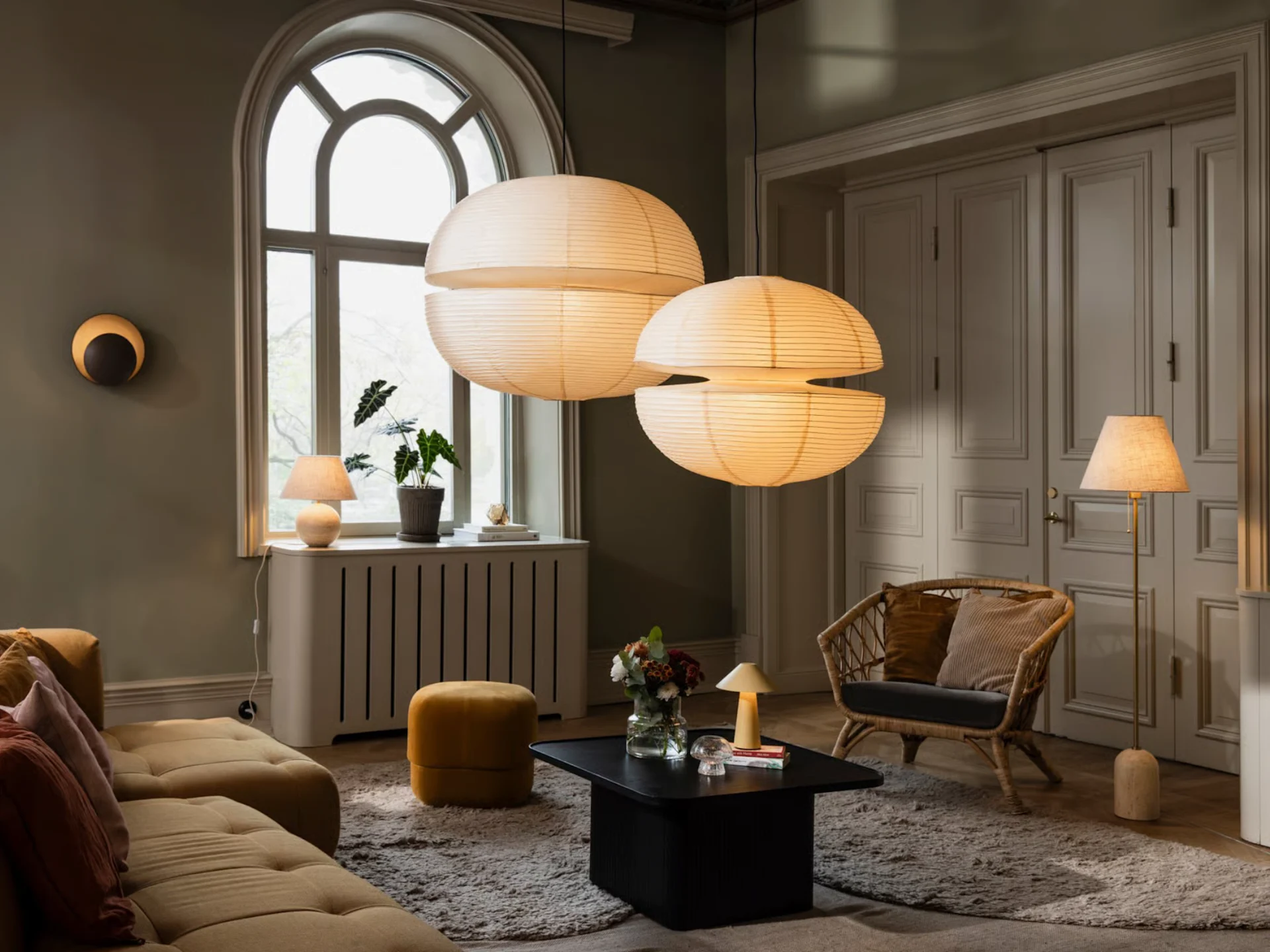두 개의 큰 종이 펜던트 조명, 노란색 소파, 등나무 의자 및 다양한 램프가 있는 아늑한 거실.